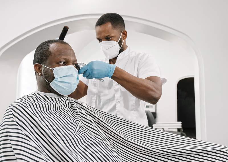 一位顾客在理发店理发. 理发师和顾客都戴着防护面具.