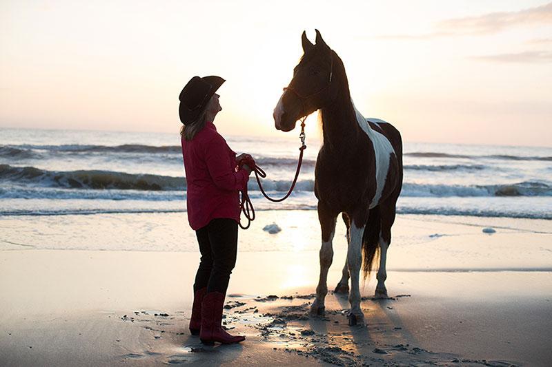 黛比和她的马在日落海滩骑马